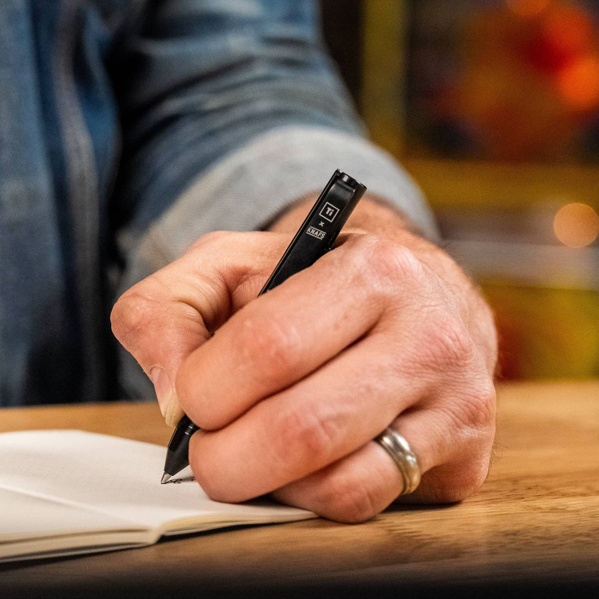 Knafs multi tool pen in black being used to write on a notebook with a hand visible