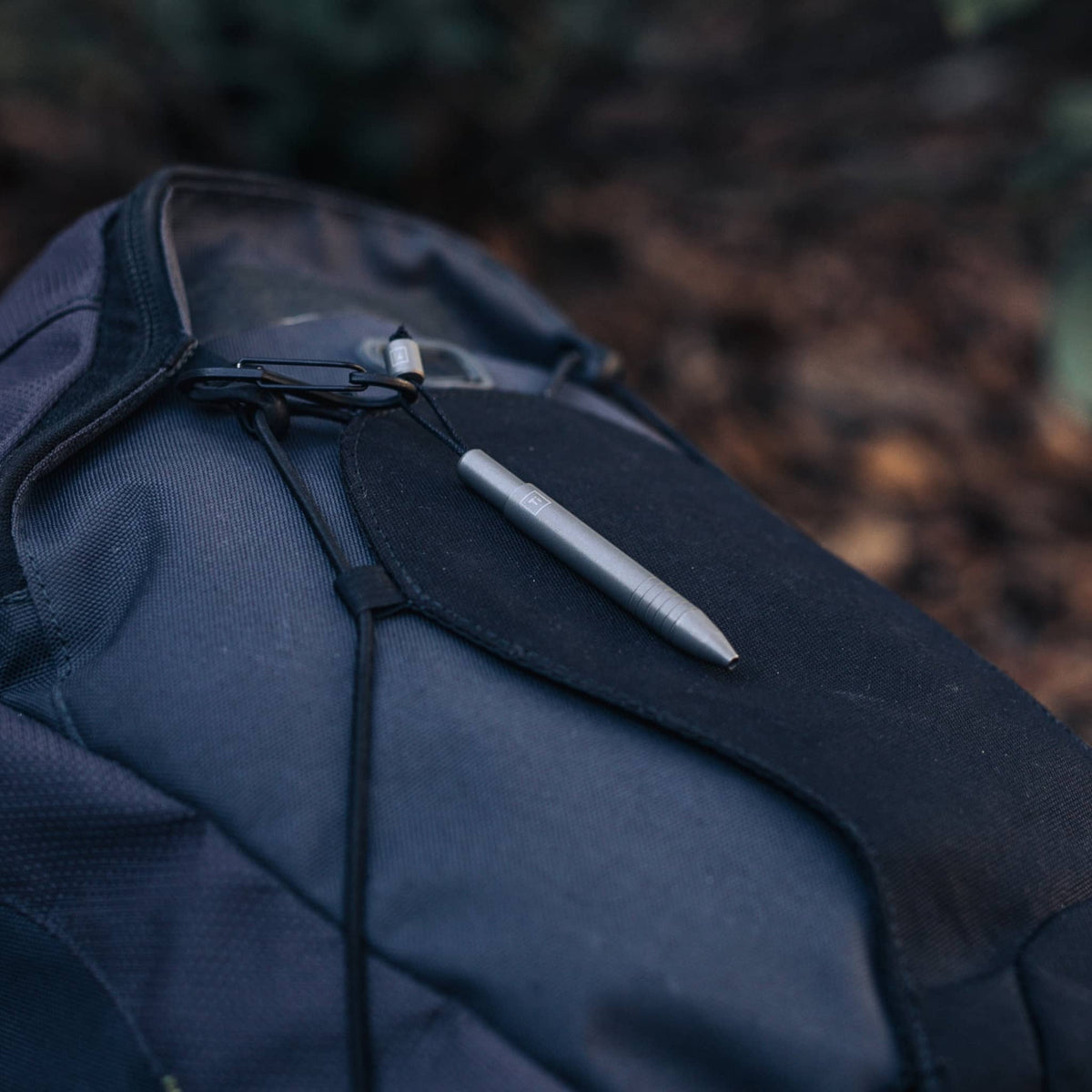 EDC titanium mini pen from Big Idea Design LLC clipped to black and gray backpack outdoors