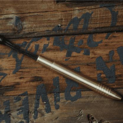 EDC titanium mini pen by Big Idea Design LLC with a brass finish and keychain loop on wooden surface