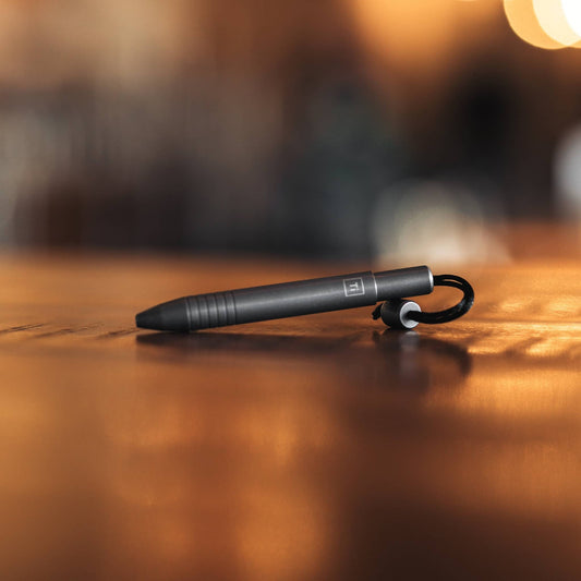 EDC titanium mini pen by Big Idea Design LLC resting on a wooden surface with a black keyring