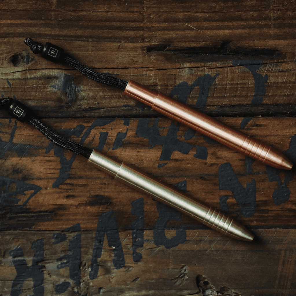Big Idea Design LLC EDC titanium mini pen in copper and brass finishes on dark wooden surface
