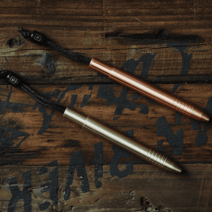 Big Idea Design LLC EDC titanium mini pen in copper and brass finishes on dark wooden surface
