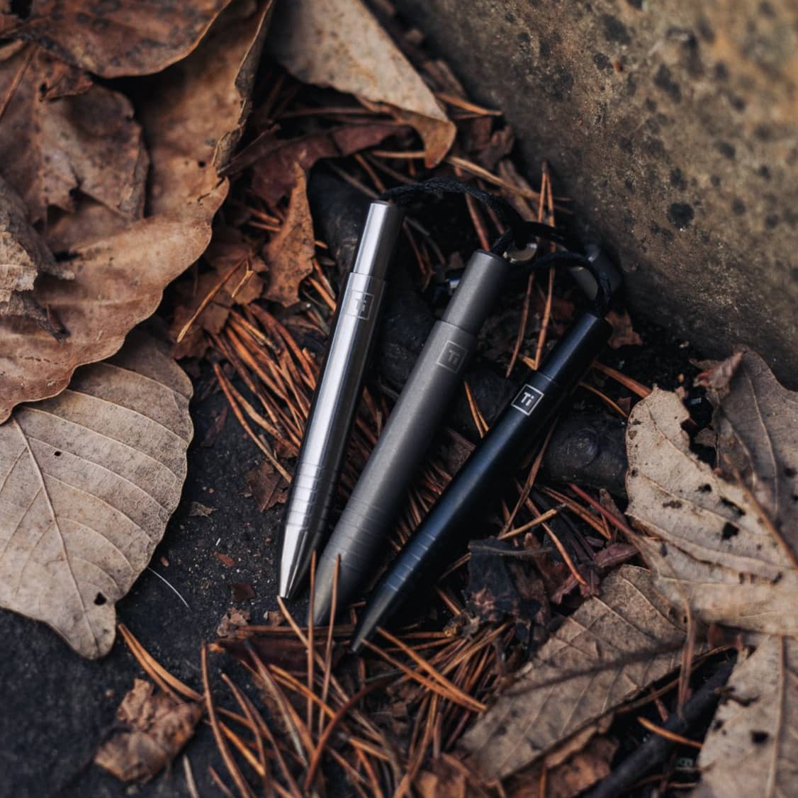 Big Idea Design LLC EDC titanium mini pen set in silver black and gray placed on dry leaves outdoors
