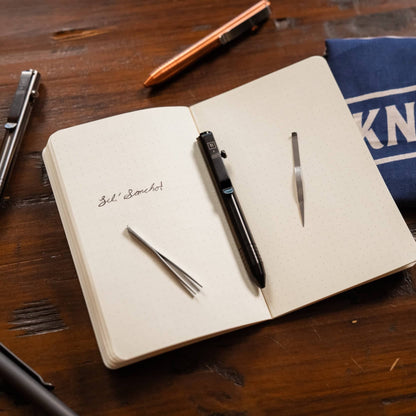 Knafs multi tool pen in black placed on a notebook with metal tools and a blue fabric Knafs pouch