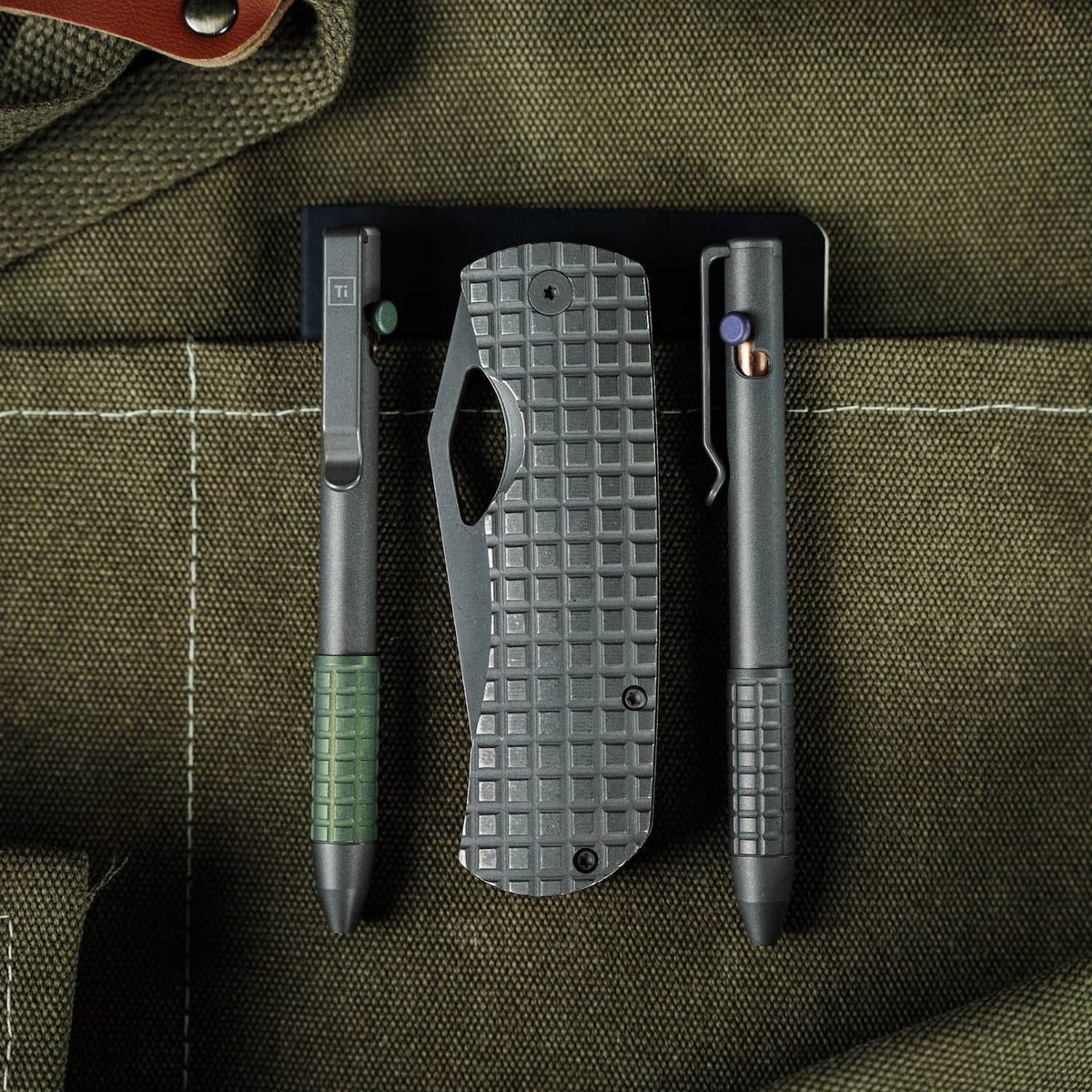 McNeese Pen in gray with ergonomic grip alongside tactical knife and accessories