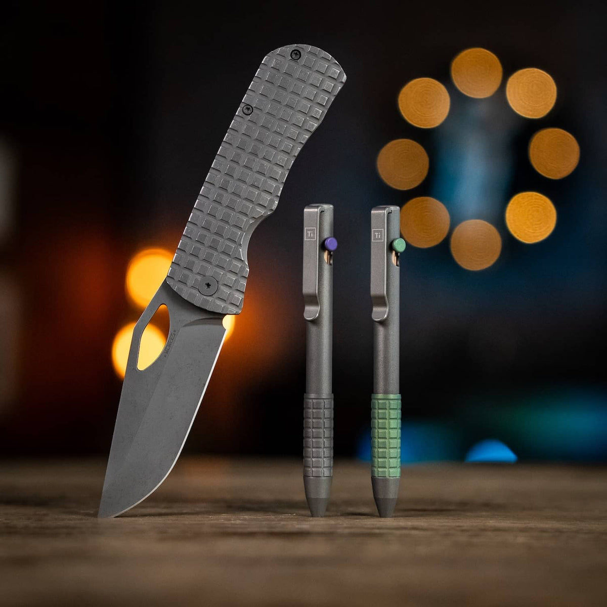 McNeese Pen in gray with textured grip, next to a gray folding knife on a wooden table