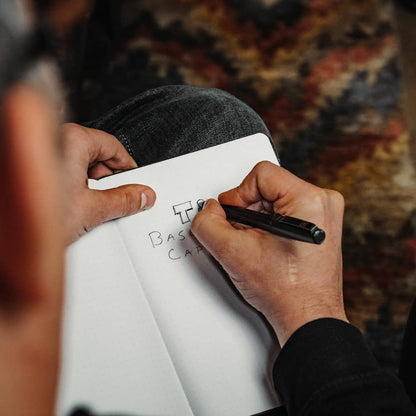 Person writing in notebook with a black titanium capped pen from BIG IDEA DESIGN LLC
