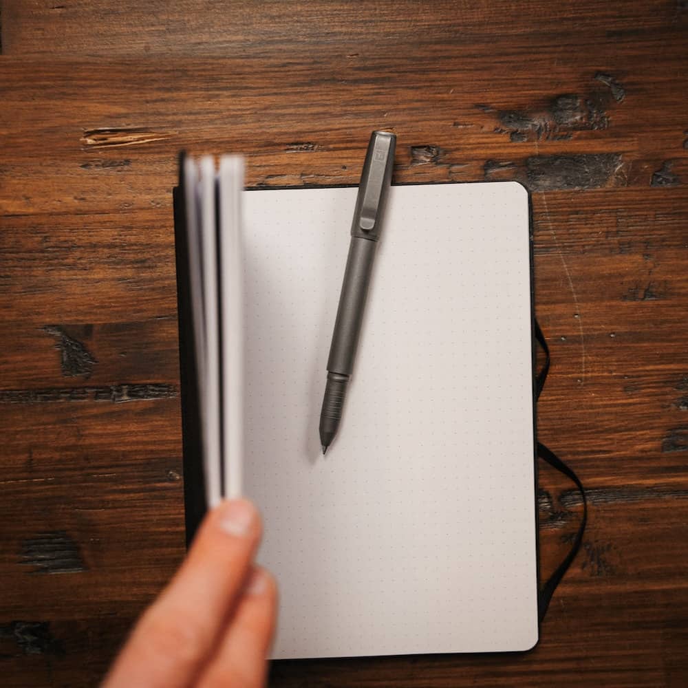 Titanium capped pen placed on an open notebook with a wooden desk background by BIG IDEA DESIGN LLC